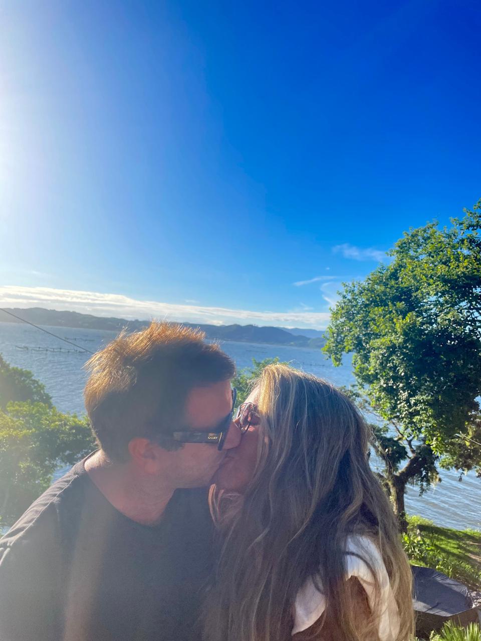 Sabrina e Raf se beijando, o sol caindo sobre a água atrás deles.